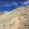 After rounding the ridge, continue on loose trail before reaching the rocky, scrambly area.