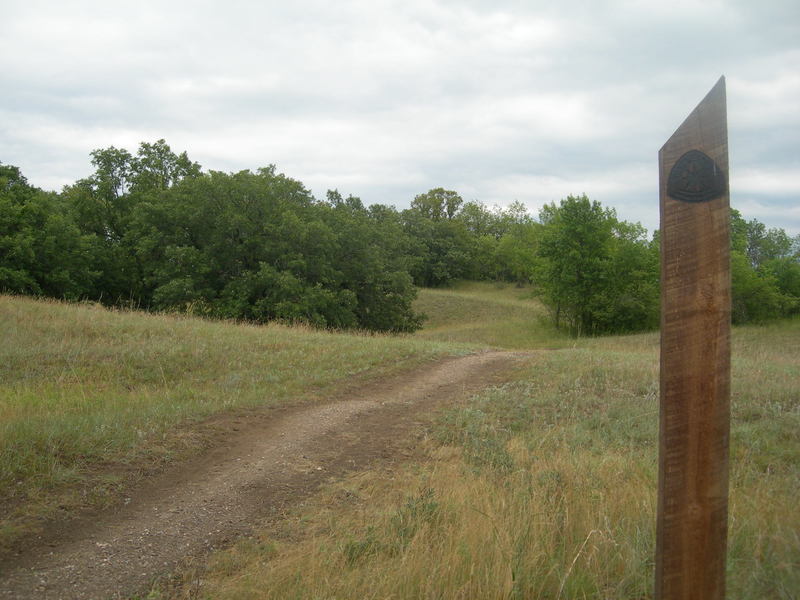 The gravel trail tread along with the angle-topped wooden marker post.