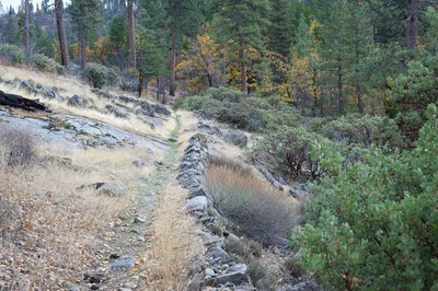 The trail skits along a rock barrier as it makes its way through an open area.