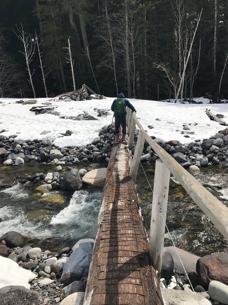 A hiker crosses the log bridge at the wonderland trailhead via Carter Falls/Longmire entrance.