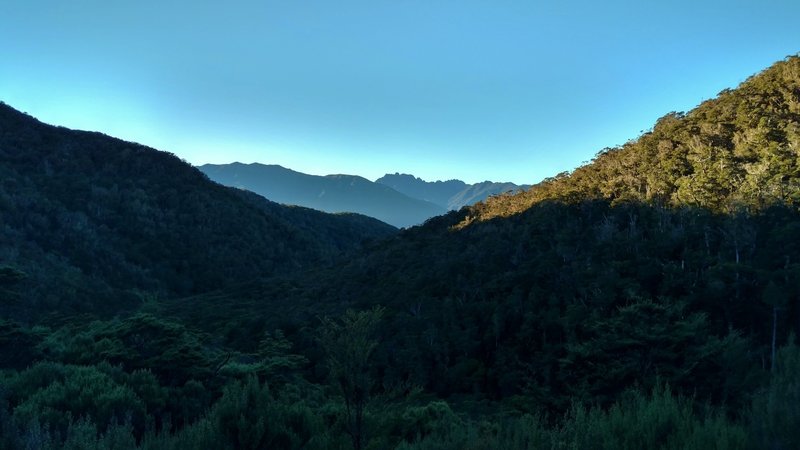 A new day dawns over the landscape on the porch of the Perry Saddle Hut on the Heaphy Track.