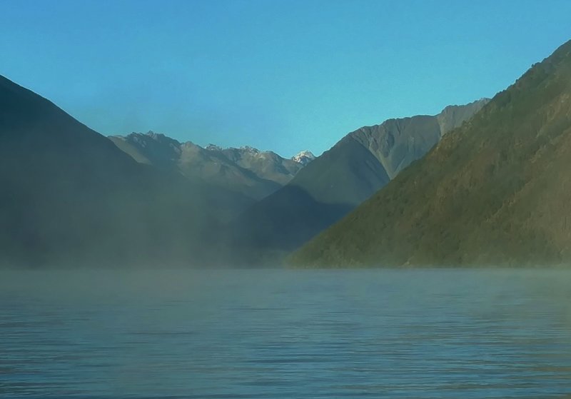 Early morning mist floats atop Lake Rotoiti with the northernmost Southern Alps in the distance.
