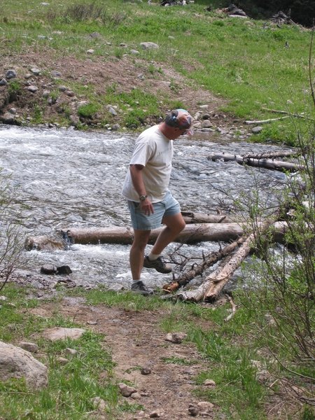 An adventurer builds and tests a log bridge to cross Little Cimarron River during spring flooding.