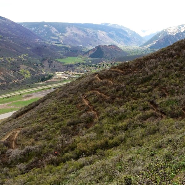 Airline Trail with tiny riders and big berm turns. Airport runway, Red Butte, and City of Aspen beyond.