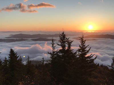 Sun rising over the cloud encased South Toe River Valley as the wind begins to whip up the just moments before still clouds as seen from Sunrise Point along the Woody Ridge Trail