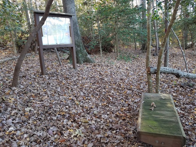 Resting bench and trail map with view of lake to the right of photo.