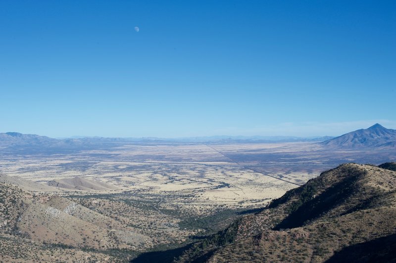 The moon rises above Arizona from the trail in the late afternoon.  You can see the 16 foot border wall stretching into the distance from the peak.