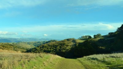 The Diablo Range can be seen in the distance looking east-northeast, just before Serpentine Loop Trail drops amid the grass and wooded hills of Calero County Park.