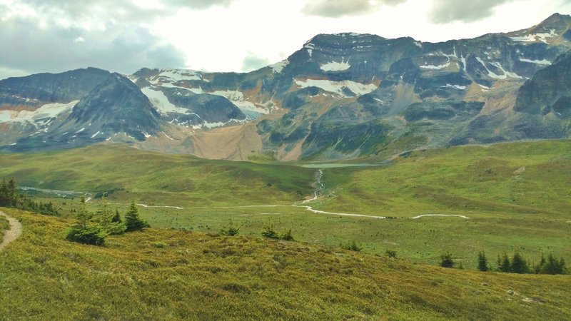 Mountains, snowfields, glaciers, and a small lake rise above the Jonas Creek valley at the creek's headwaters. Seen just below Jonas Shoulder when looking west.