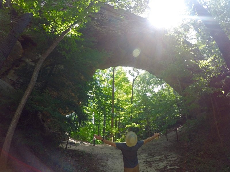 A hiker basking in the sunlight and the size of the arch.