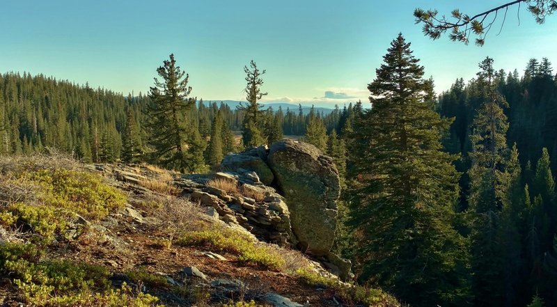 Fir forested hills stretch into the far distance when looking southeast from a rocky bluff in a remote area near the southern border of Lassen Volcanic National Park, along Twin Meadows Trail.