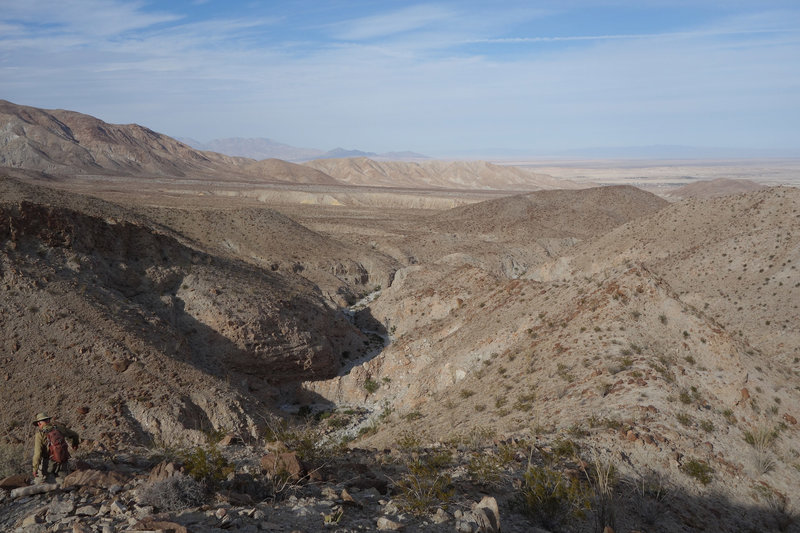 Hiker descending the ridge above Lyceum Wash. Hike drops rightward at the saddle at the lower right.