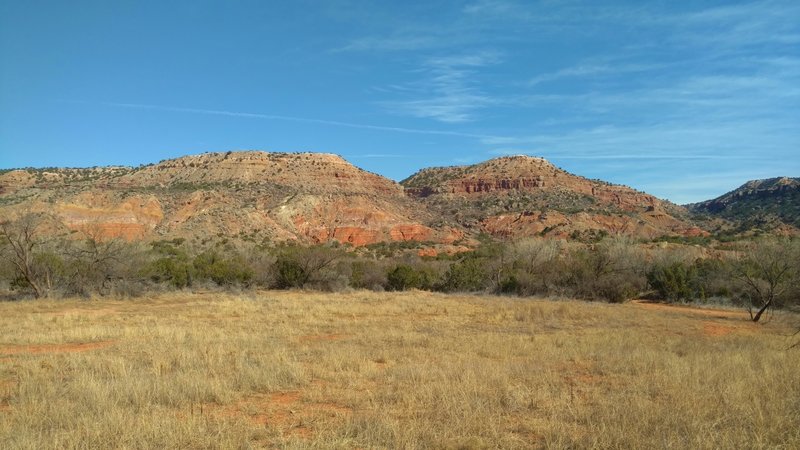 Fortress Cliffs and their beautiful orange, white, beige, purple, and gray layers, behind a small meadow passed by Pioneer Nature Trail.