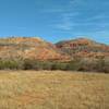 Fortress Cliffs and their beautiful orange, white, beige, purple, and gray layers, behind a small meadow passed by Pioneer Nature Trail.