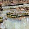 What mineral is causing the cloudy white appearance of the streams seen on this trail?