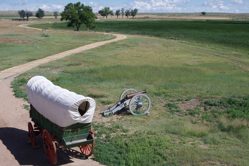 A wagon and canon sit alongside the paved walkway that leads to the visitor parking area.