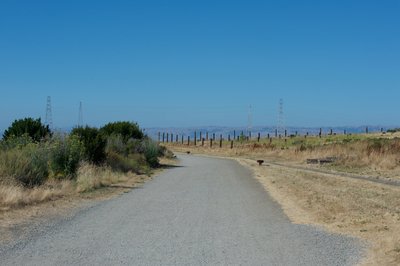 The trail departs the parking lot via a wide, gravel trail that leads out to the South San Francisco Bay.