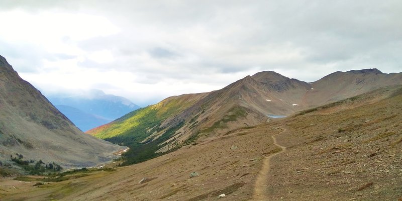 A sunlit creek valley (left) is where Curator trail camp is found. Curator Lake (center right) in the distance is where Skyline Trail is headed as it heads north on the barren, alpine north side of Big Shovel Pass.