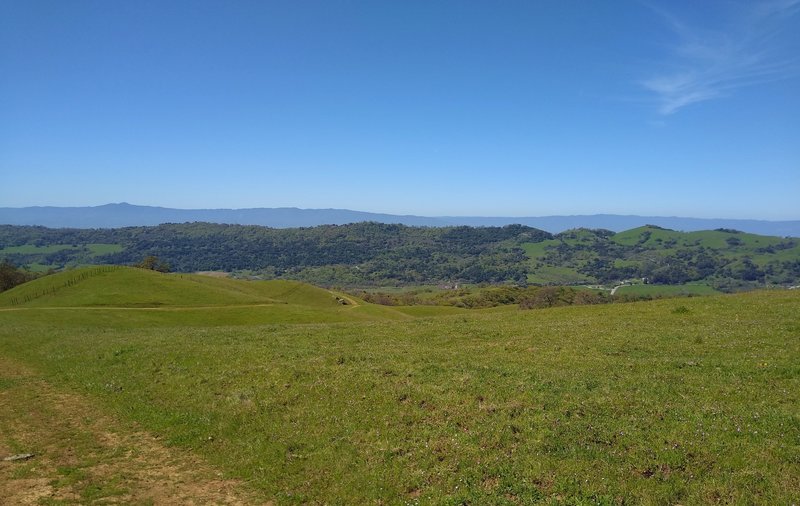 The blue Santa Cruz Mountains are in the distance with Loma Prieta, 3,790 ft., the highest, on the left. Nearer, are the spring green hills of Joseph D. Grant County Park.  Seen looking southwest from high on Los Huecos Trail.