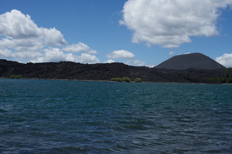 Cinder Cone rises in the distance as the Fantastic Lava Beds come right up to the water.  Kayakers, paddleboarders, and fishermen can be seen on the lake.