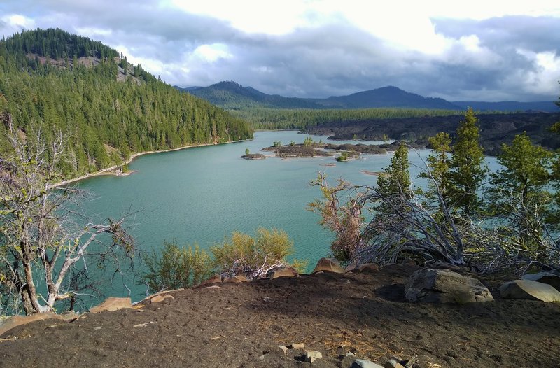 Rising above Butte Lake (left to right) are Sunrise Peak, Ash Butte, and Mt. Hoffman. The islands and boulders on the right shore are fantastic lava beds from slow cooling lava of cinder cone eruptions. Looking south from the north end of Butte Lake.