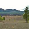 Light colored Painted Dunes (center) at the base of Cinder Cone (north side) on the right, with the black boulders of Fantastic Lave Beds behind them. In the distance are Ash Butte (left), Red Cinder Cone/Red Cinder (center), and Mt Hoffman (right).