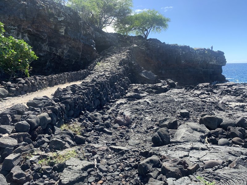 A slight incline along the 1871 trail leading up to a rocky outcrop above the Pacific Ocean.