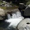 A small waterfall above the swinging bridge flows fast even in the summer.