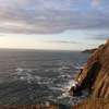 A sea cliff with waves crashing against it close to sunset.