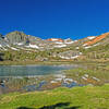 The first of the 3 Frog Lakes. Some of the mineral rich soils appear brilliant orange in direct morning or evening sunlight. Burro Pass in the low point in the ridge in front of the orange mountain.