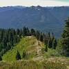 A bird's eye view of Wenatchee Ridge Trail below from a lookout up higher along the trail.  Rugged mountains stretch into the far distance in all directions.