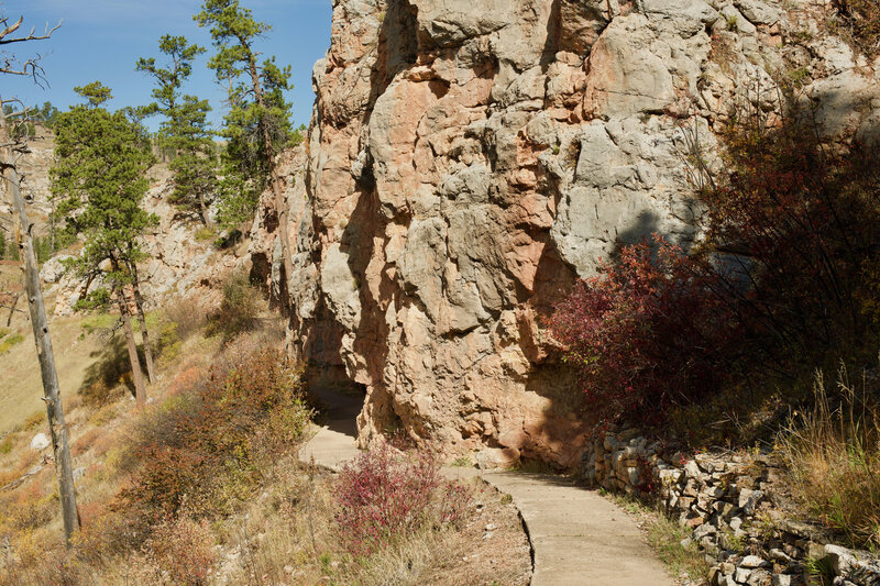 The trail turns to pavement as it runs along the rock outcrops and a cave entrance.