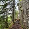 View up the trail along a large steep wall of rock.