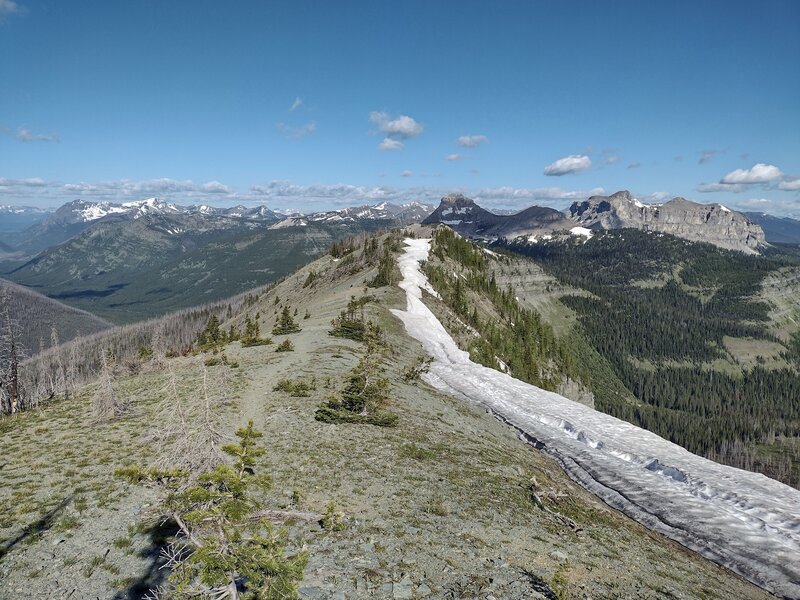 The trail runs on a high ridge of the Great Divide here, with a slow melting cornice to the right, cracked, could fall down the cliff. In the distance are Font Mountain (right center) and Mount Matkin (right). Seen looking west-northwest.