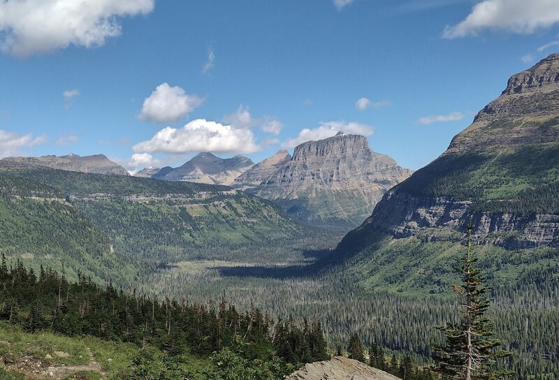 Citadel Mountain (right) nearby, Going-to-the-Sun Mountain (center right) distant, Fusillade Mountain northeast shoulder stretching from center to left across the valley.  Headwaters of St. Mary River run through the valley. Seen looking northeast.