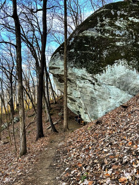 Two folks sitting below a massive boulder.