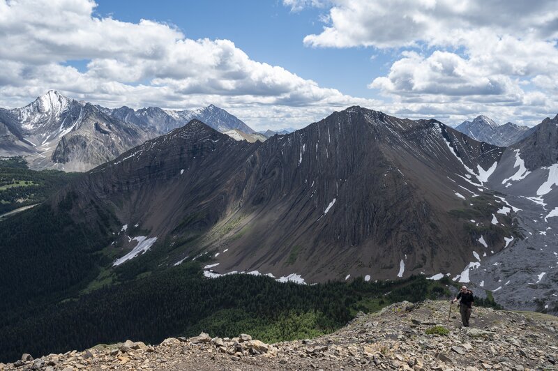 A hiker ascends the south Pocaterra Ridge, Highwood Ridge in the background.