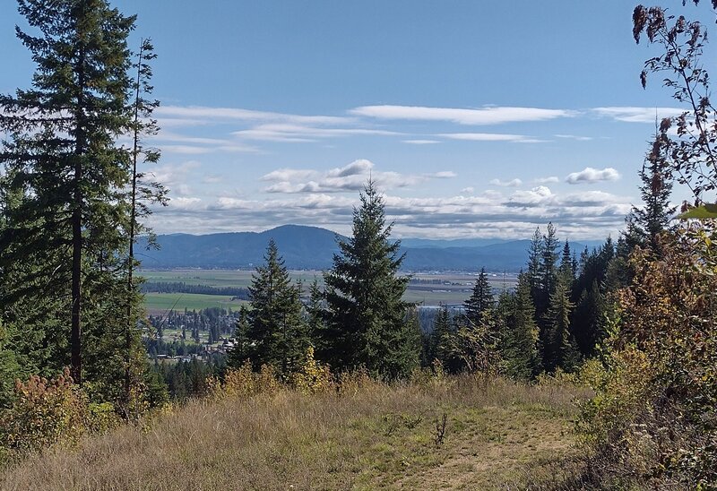 Farms in the valley below with a backdrop of distant, forested mountains.