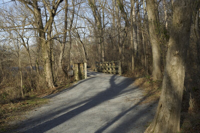 The trail is crushed gravel and crosses a wooden bridge over a small creek that breaks off from the main river.