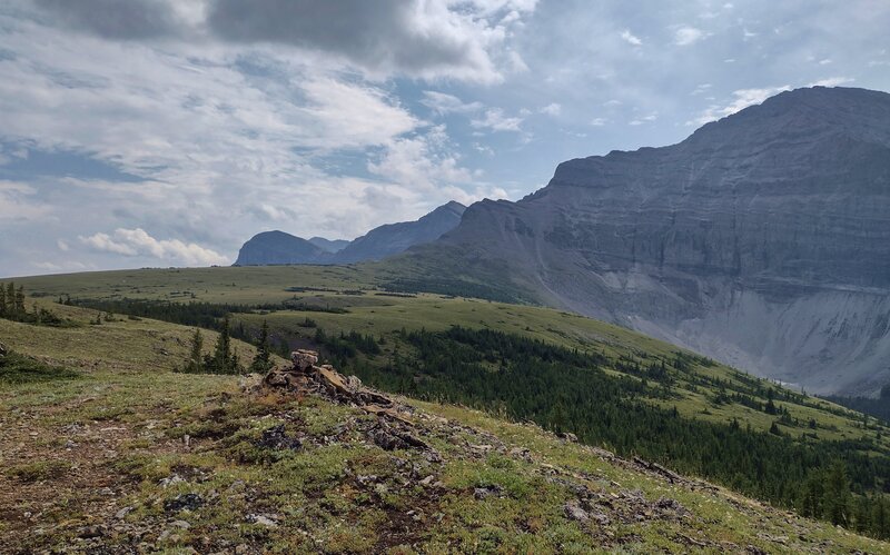High meadows and peaks of the Great Divide. The Great Divide Trail passes a little cairn (lower left) just before it begins its descent into a small creek valley below.