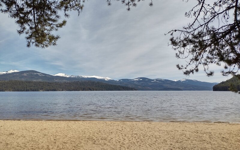 Mountains of the Selkirk Crest are seen across Priest Lake, when looking east from the sandy beach by Elkins Resort at the north end of Kalispell - Reeder Bay Trail.