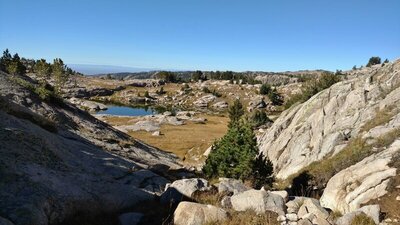From high on Doubletop Mountain Trail, one can see all the way to the flat lands, to the west. Nearby, typical of this area, is the rocky, grassy terrain dotted with trees and a cute lake.