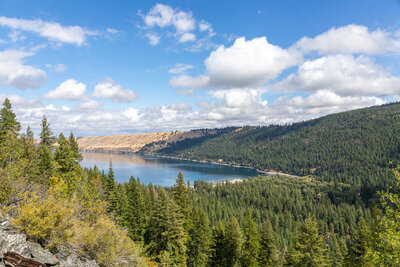From a rocky viewpoint at 5,450 ft, the southern shore and sandy beach of Wallowa Lake are framed by the sweeping expanse of the East Moraine as its dense conifer forest transitions into golden bunchgrass slopes.